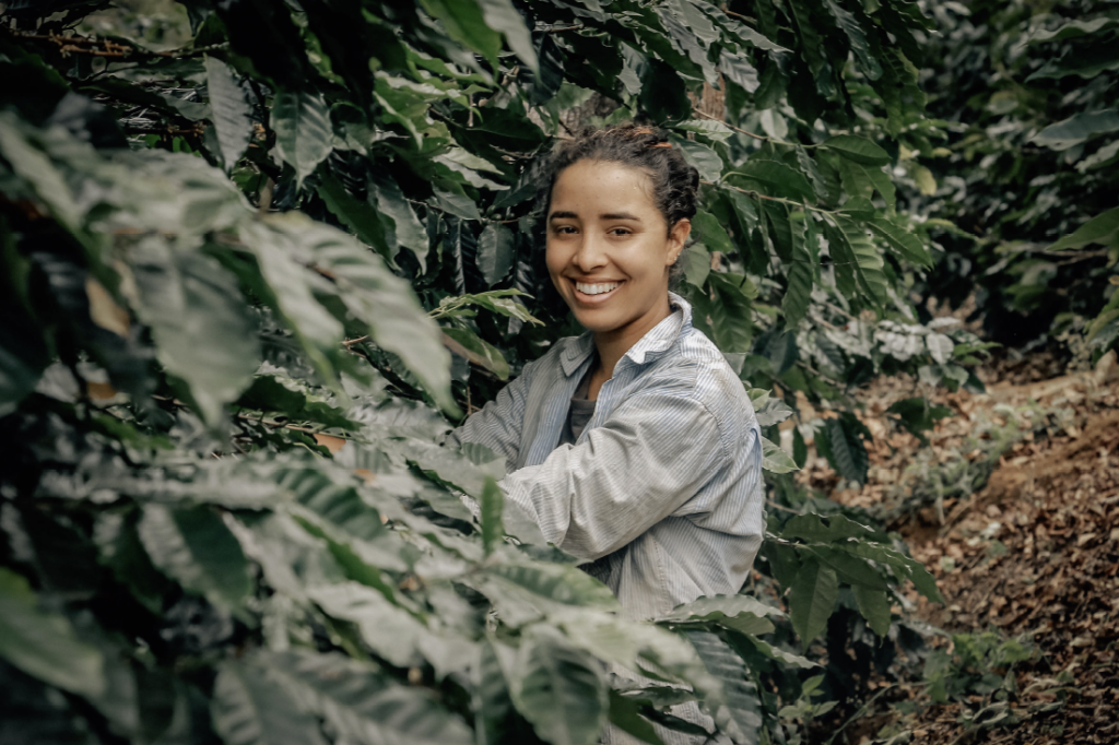 Uma mulher sorrindo, perto de um pé de café.